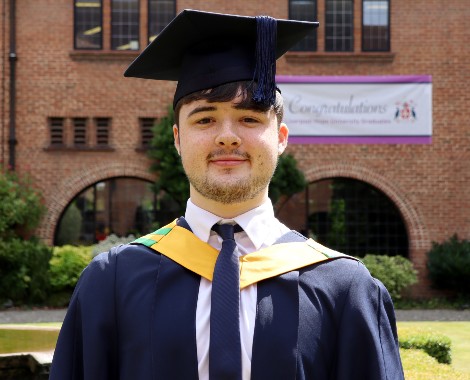 Male student wearing graduation cap and gown over shirt and tie.